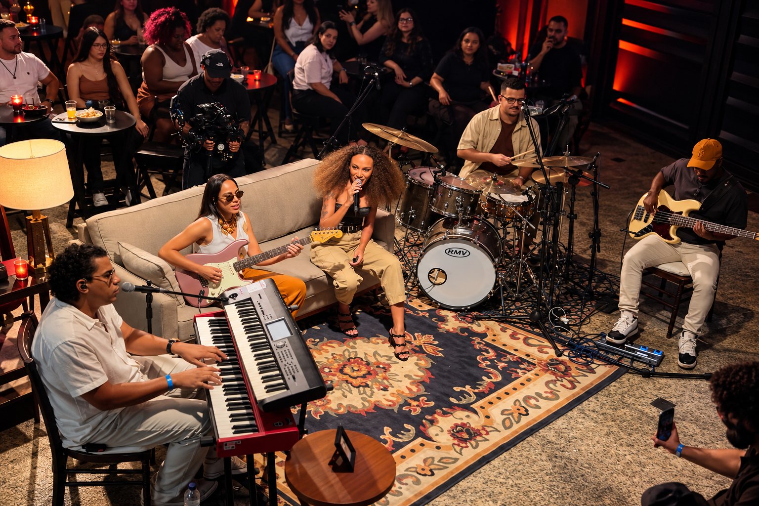 Banda tocando ao vivo no salão da Arena Billboard, com cantora ao microfone, teclado, bateria e baixo, cercada pelo público sentado às mesas.